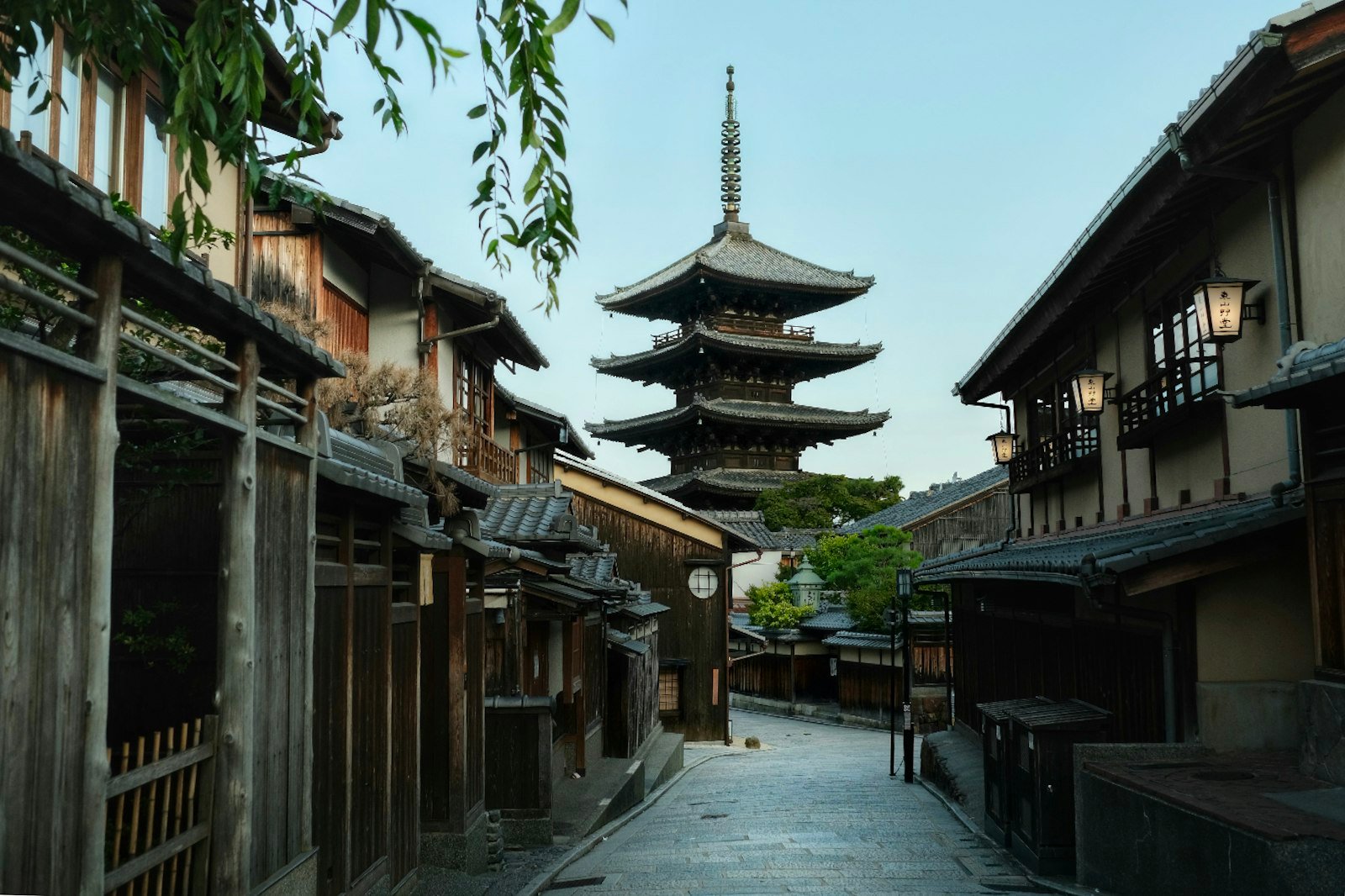 An empty stone lane lined with dark wooden houses leading to the five-storey Yasaka pagoda at dawn in Kyoto
